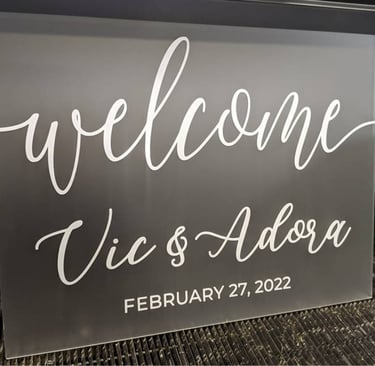 Gray acrylic welcome sign with 'Vic & Adora, February 27, 2022' in white script, ready for a wedding