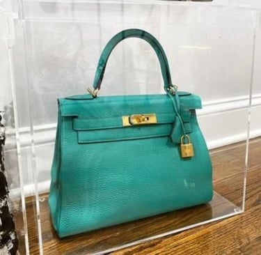 Teal designer handbag showcased in clear acrylic box.