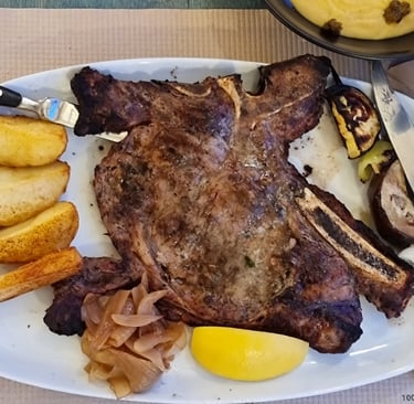 Grilled t-bone steak served with potato wedges, caramelized onions, and a side of creamy polenta.