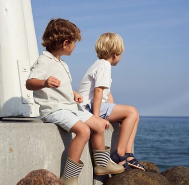 Wheat SS25 campaign imagery featuring 2 young boys sitting by the sea, wearing Wheat clothing and footwear