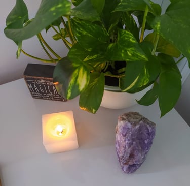 um cenario de uma vela, cristal ametista e uma planta em cima de uma mesa
