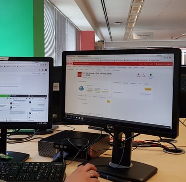 a woman sitting at a desk with two monitors and a keyboard