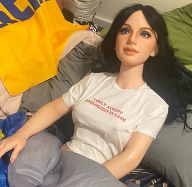a sex doll posed in bed covered by a blanket