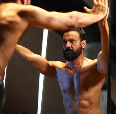 Shirtless man looking in mirror and evaluating himself and thinking about his fitness