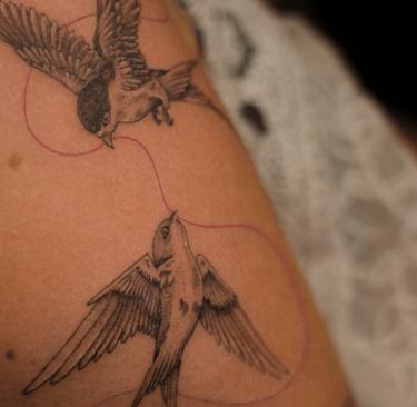 Tatouage d'oiseau avec un fil rouge sur le bras réalisé par Eva Ink Vlr