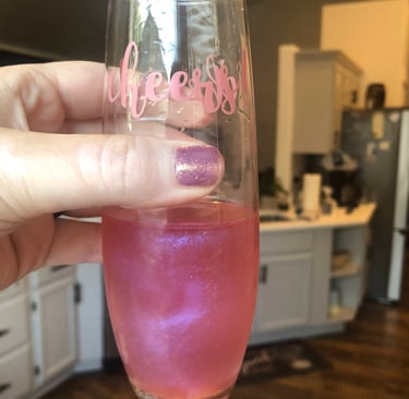 a person holding a wine glass with a pink edible glitter in their drink
