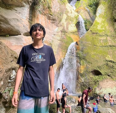 Un joven viajera posando frente a una majestuosa cascada escalonada que fluye sobre acantilados 