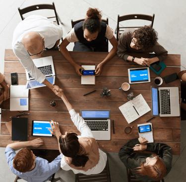 a group of people sitting around a table with laptops