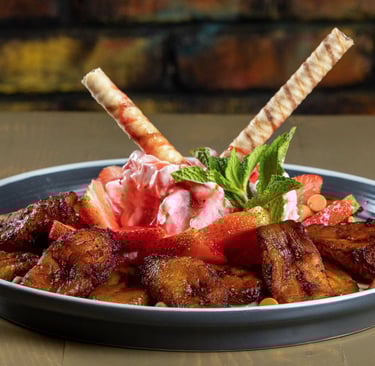 Postre de plátanos fritos con fresas, helado de fresa, barquillos y hojas de menta.
