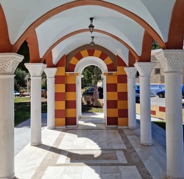 Greek Orthodox church arcade with white marble columns and arched hallways in a sunny courtyard.