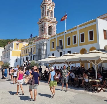 Panormitis Monastery clock tower and courtyard with tourists on Symi Island, Greece.