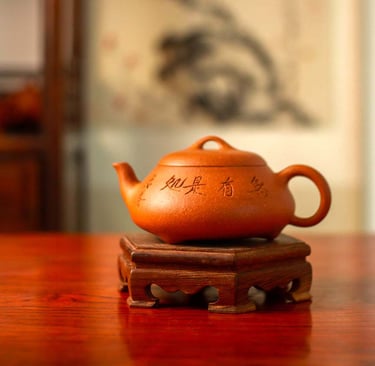 A yellow Yixing teapot engraved with Chinese characters is placed on a wooden stand