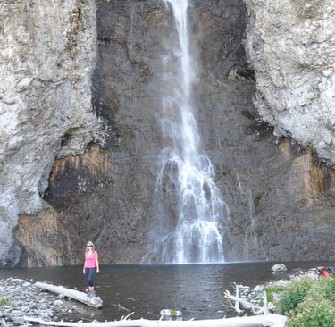 a woman standing in front of Fairy Falls waterfall in Yellowstone National Park