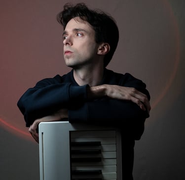 Arnavall debout appuyé sur un piano, de face