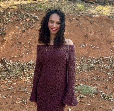 a woman in a brown crochet dress standing in front of a wooded area