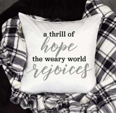 A throw pillow on a black & white checked throw over a black chair. Pillow reads, "A thrill of Hope the weary world Rejoices.