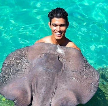 a man in a swimsuit is smiling and holding a stingperk dolphines punta cana