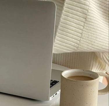 Woman in a cozy cream sweater working on a laptop with a coffee mug on the desk.