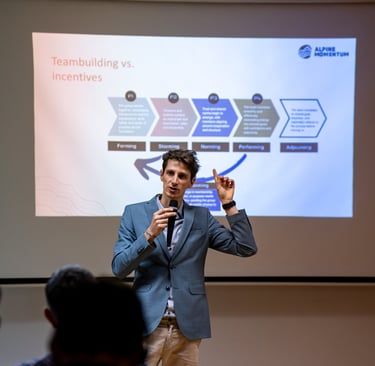 A male speaker presenting Tuckman's stages of team development at a corporate teambuilding workshop.