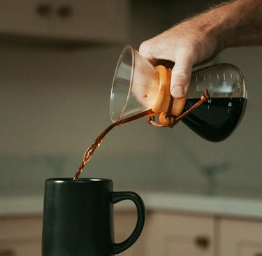 Mano sirviendo café filtrado en una taza negra usando chemex, mostrando métodos de preparación artes