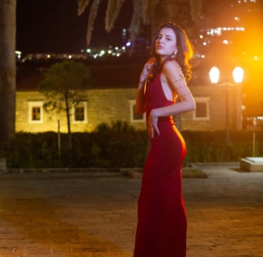 Elegant woman in form-fitting red evening dress poses in historic stone alleyway of Old Town Budva