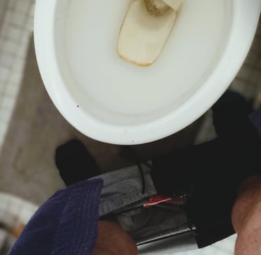 a male holding his penis over a toilet bowl on white tiles