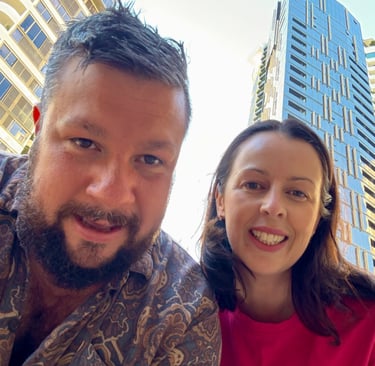 Two people smiling outdoors with modern city buildings in the background