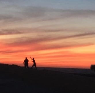 A picture showing an enchanting silhouette of three people being playful while enjoing the sunset.