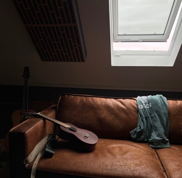 Guitar resting on leather couch under roof window in studio room