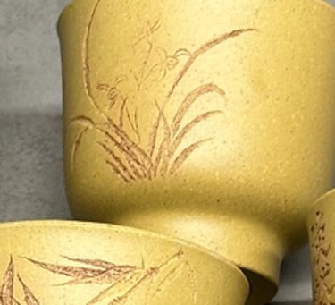 Three yellow teacups engraved with artwork, with an ancient stone beside them