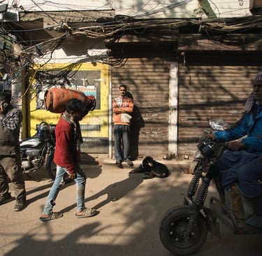 Pedestrians and a motorbike passing closed shops on an Old Delhi street.