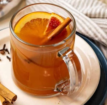 a clear glass mug filled with hot apple cider, orange slice and cinnamon stick garnish