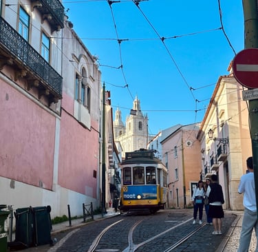 Uma estrada estreira entre as casas portuguesas, com um bondinho ao meio e a catedral ao fundo.