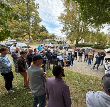 a group of people standing around a table with a car in the background