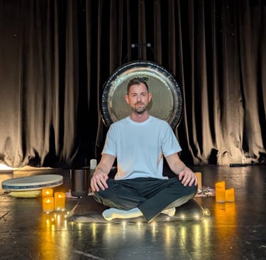 a man sitting in front of a gong leading a relaxing sound bath