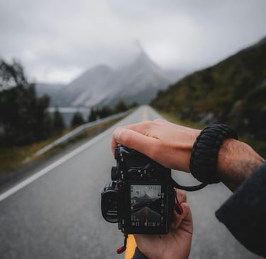 a person holding a camera taking a picture of a vast open road in the mountains
