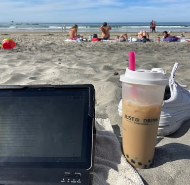 a laptop computer and a cup of brown sugar milk tea with boba sitting on a beach