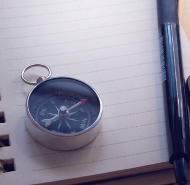 Image of compass on top of a notebook, with a pen