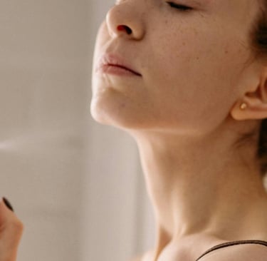 a woman in a brown tank top spraying a facial mist on her face