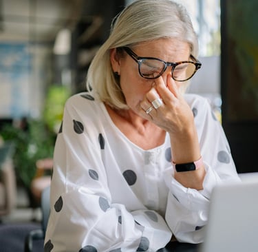 Anxious woman sits at her computer rubbing her eyes with tension