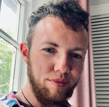 White trans masc with blue eyes, and curly light brown/auburn hair and beard. 