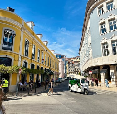 Prédios, um estrada, pessoas em bares e um tuk tuk