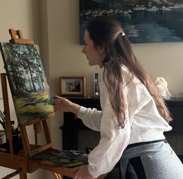 Angela Moiseieva painting at her easel in a bright art studio.
