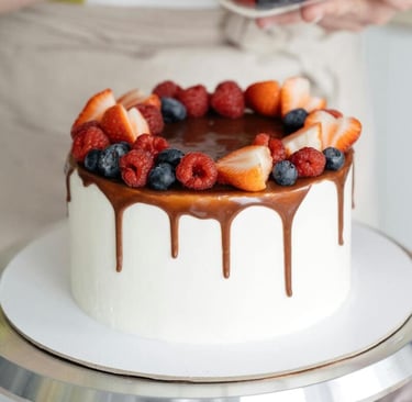Repostero decorando una drip cake blanca con frutos rojos frescos