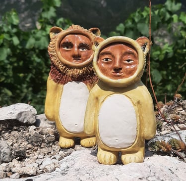 two ceramic figurines, lion and lioness smittie, on a rock in front of a mountain