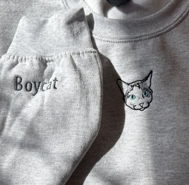 a light gray sweatshirt with a picture of a cat embroidered on it