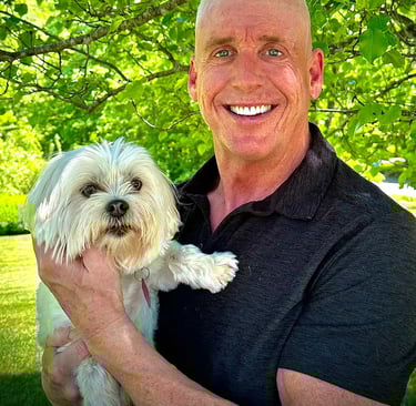 a man in a black shirt is holding a white dog; Tom O'Brien, Owner, Tymeless Properties