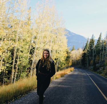 lady walking on a road with a forest and mountains in the backgroun