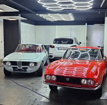 Zwei klassische Sportwagen (rot und weiß) in einer Werkstatt oder Ausstellungshalle.