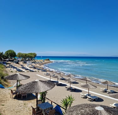 Sunny beach resort in Rhodes with straw umbrellas and lounge chairs by the blue Aegean Sea.